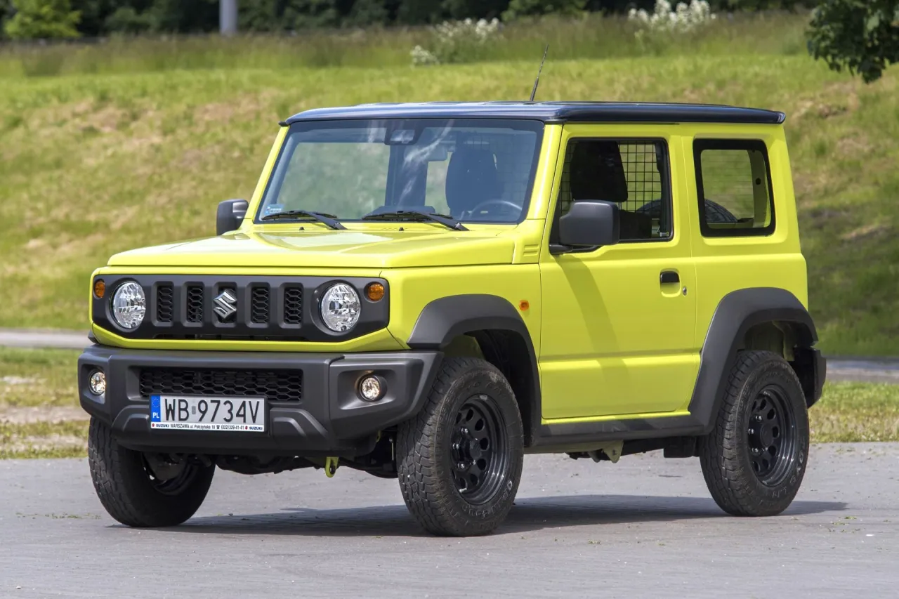 Żółty Suzuki Jimny na tle zieleni. Ten terenowy samochód, znany z niewielkiej pojemności baku, jest gotowy na przygodę.