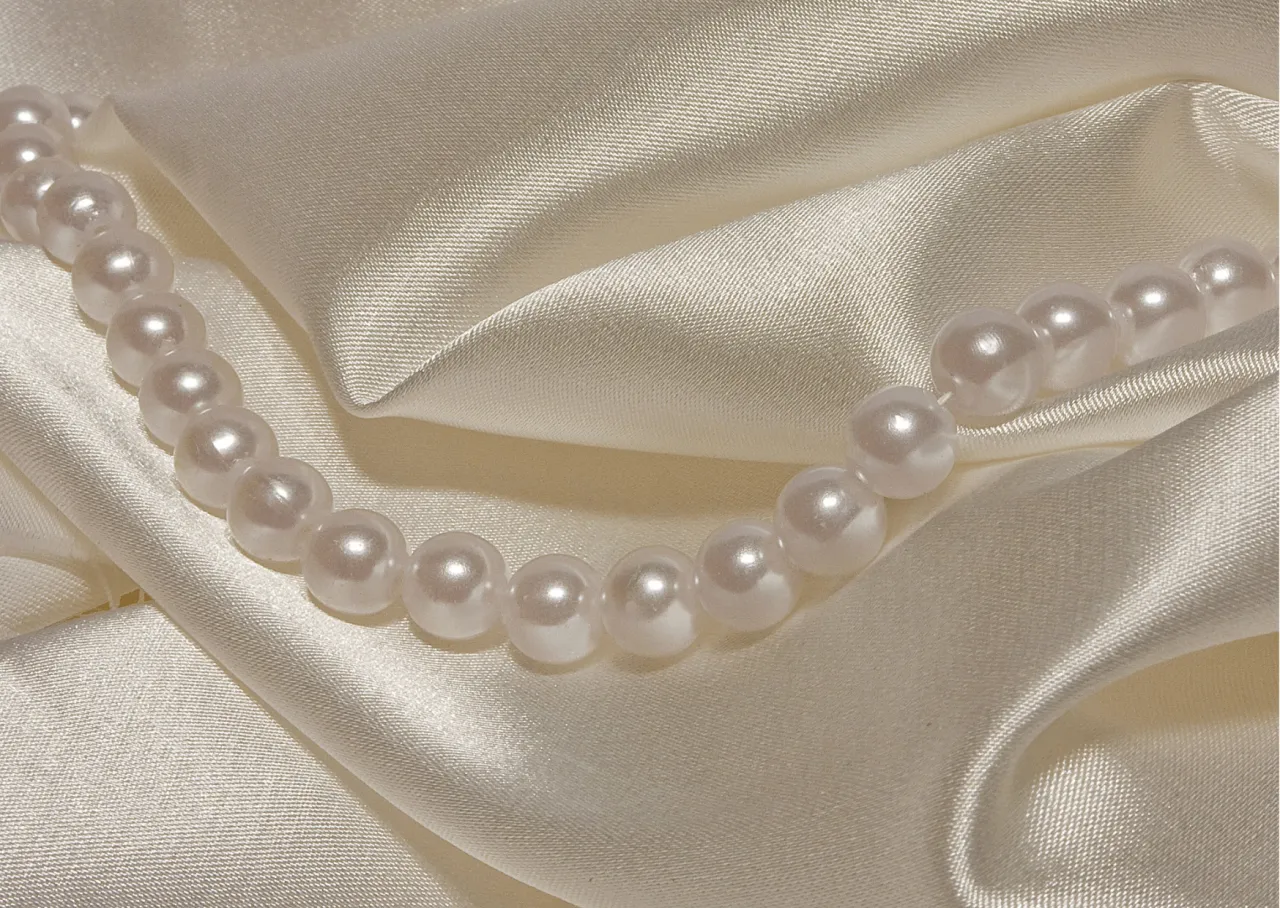 Perły na kremowym jedwabiu. Delikatne fałdy materiału i połysk pereł pomagają zrozumieć, jak rozpoznać jedwab.