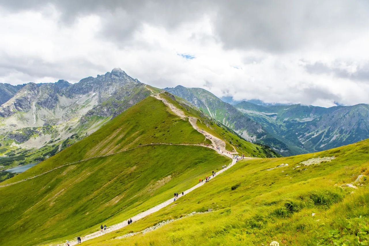 Szlak turystyczny w Tatrach, jeden z 7 najpiękniejszych miejsc w Polsce. Zielone zbocza, skaliste szczyty i chmury na niebie.