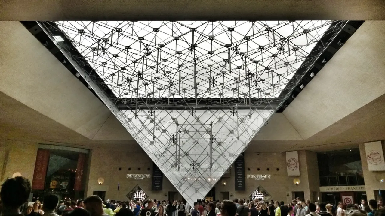 Wielka szklana piramida Luwru, pod którą tłoczą się turyści. Zastanawiasz się, ile czasu zwiedza się Luwr?