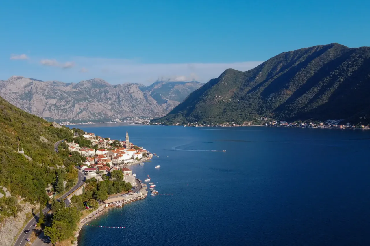 Widok na malowniczą zatokę w Czarnogórze, z krętą drogą prowadzącą do urokliwego miasteczka z białymi domami i czerwoną dachówką.