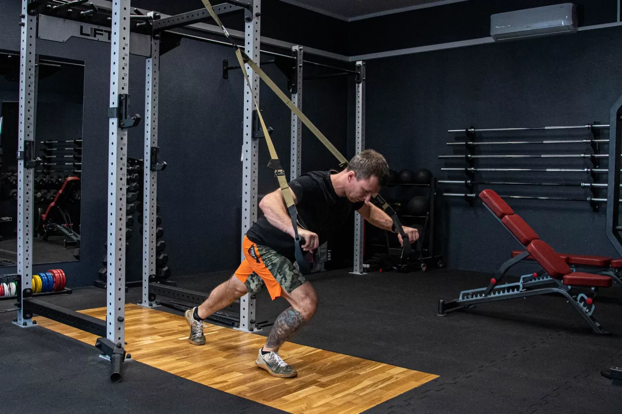 Mężczyzna ćwiczy z taśmami TRX, co jest świetnym sposobem, by zacząć trening na siłowni.