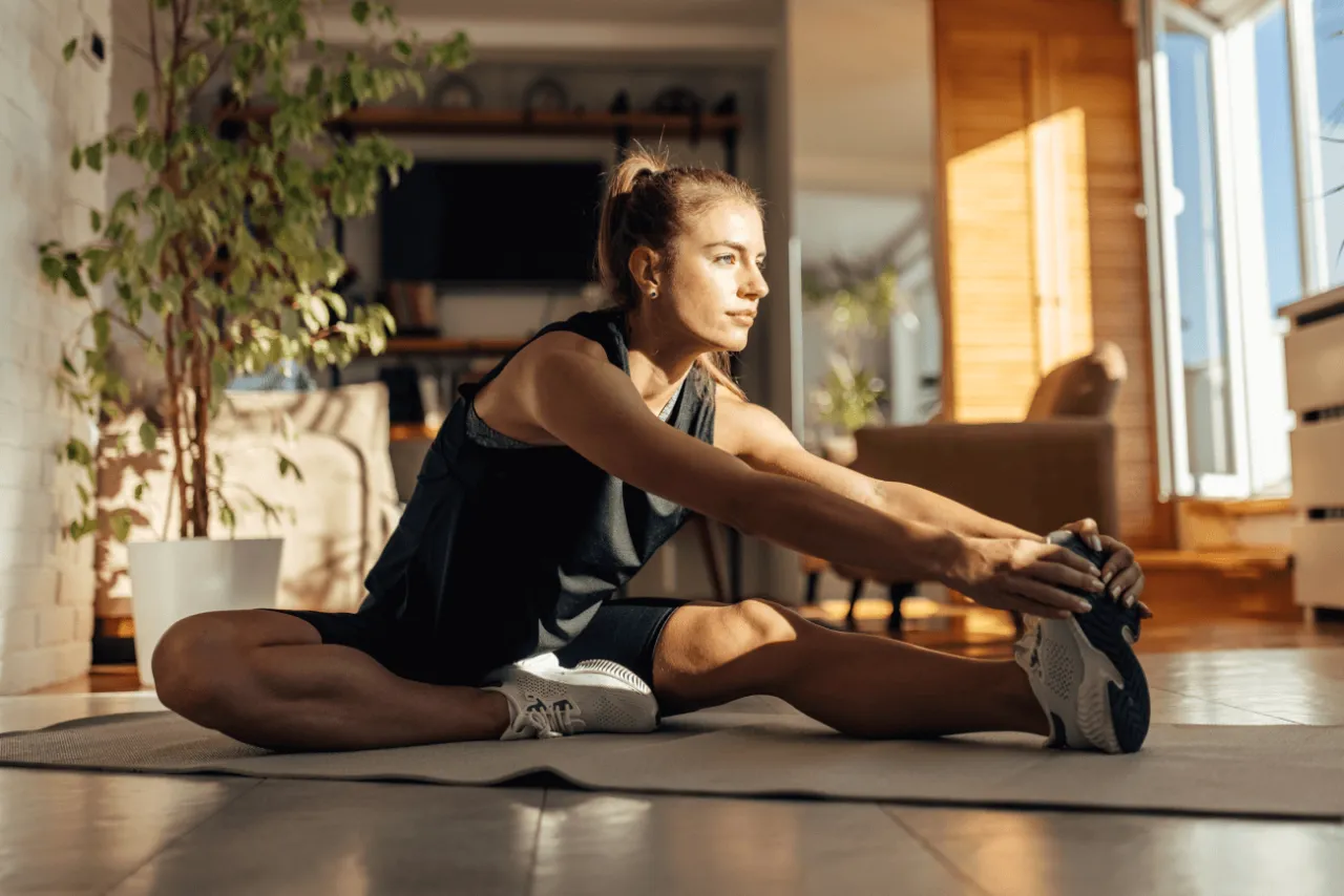 Kobieta ćwiczy w domu, wykonując rozciąganie. Idealny trening na redukcję tkanki tłuszczowej zaczyna się od rozgrzewki i rozciągania.