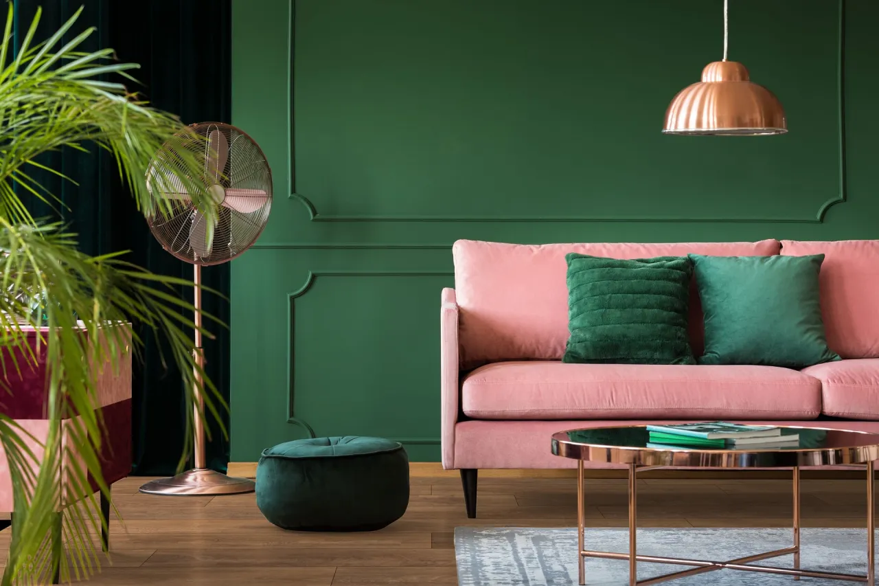 Różowa kanapa z butelkową zielenią na ścianie i poduszkach. Idealne połączenie, by stworzyć przytulne wnętrze.