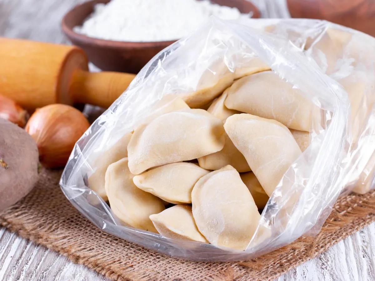 Gotowe pierogi w woreczku, idealne do pakowania pr&oacute;żniowego. Obok składniki: ziemniaki, cebula, mąka i wałek.