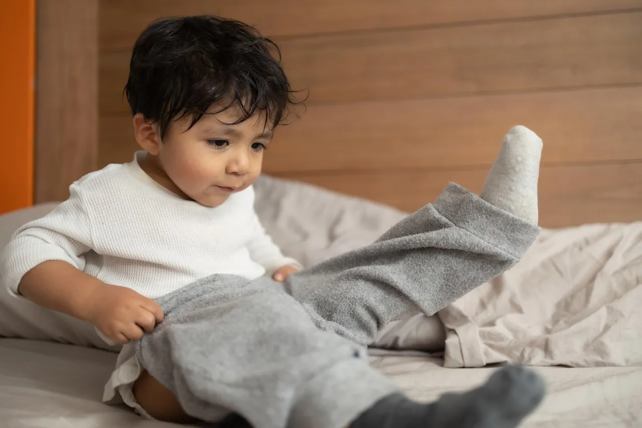 Małe dziecko, może 5 lat, próbuje samo założyć spodnie, siedząc na łóżku.