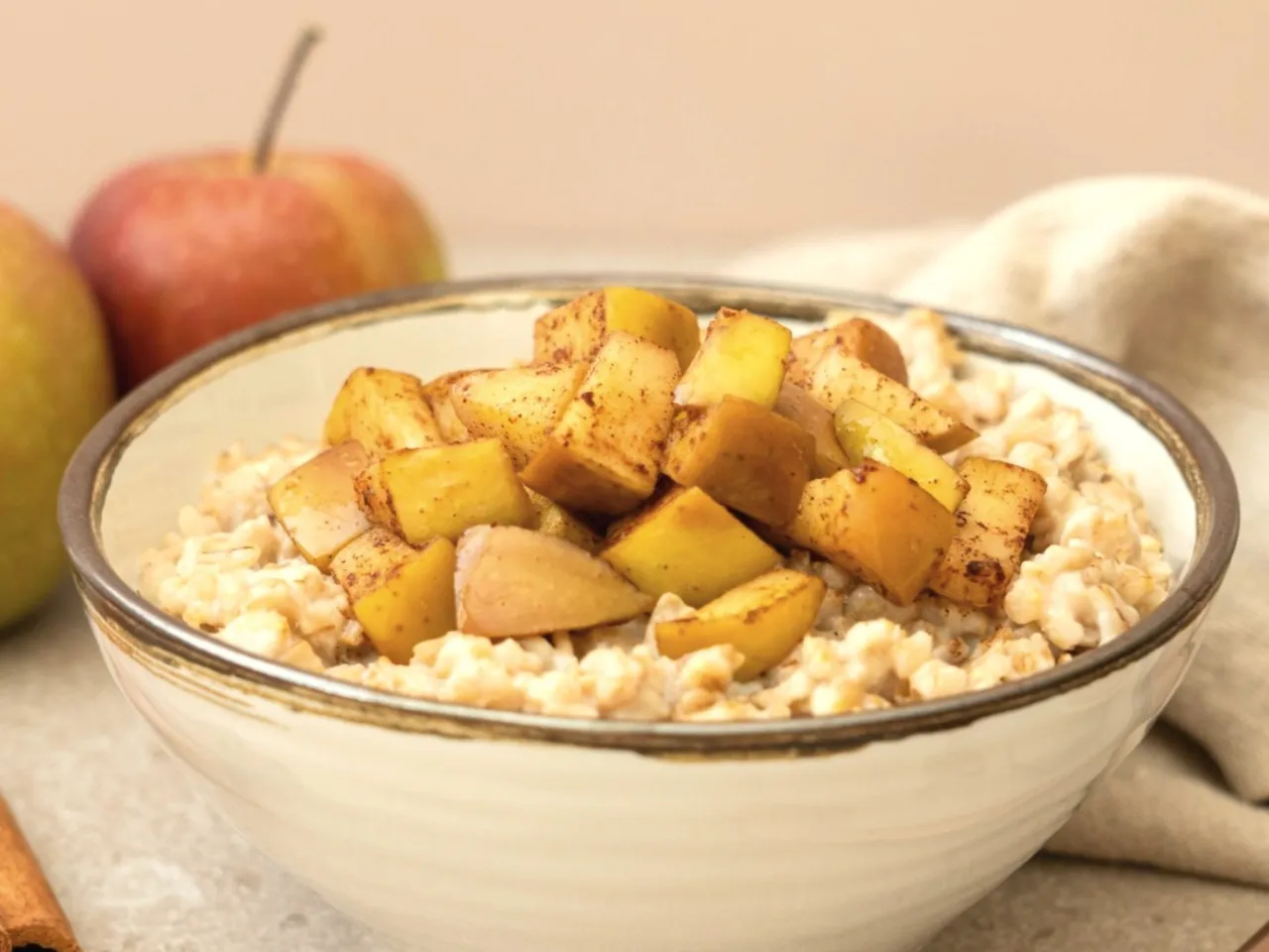 Miseczka owsianki z jabłkami i cynamonem, obok jabłka i laska cynamonu.