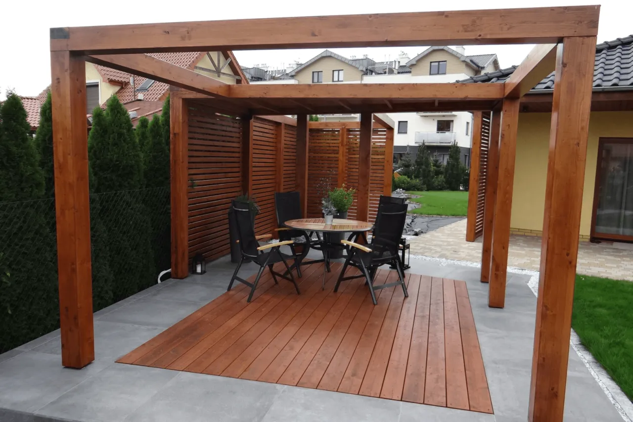 Drewniana pergola z miejscem do siedzenia i stołem, idealna na taras. Zastanawiasz się, co na pergolę w ogrodzie? Oto gotowe rozwiązanie!