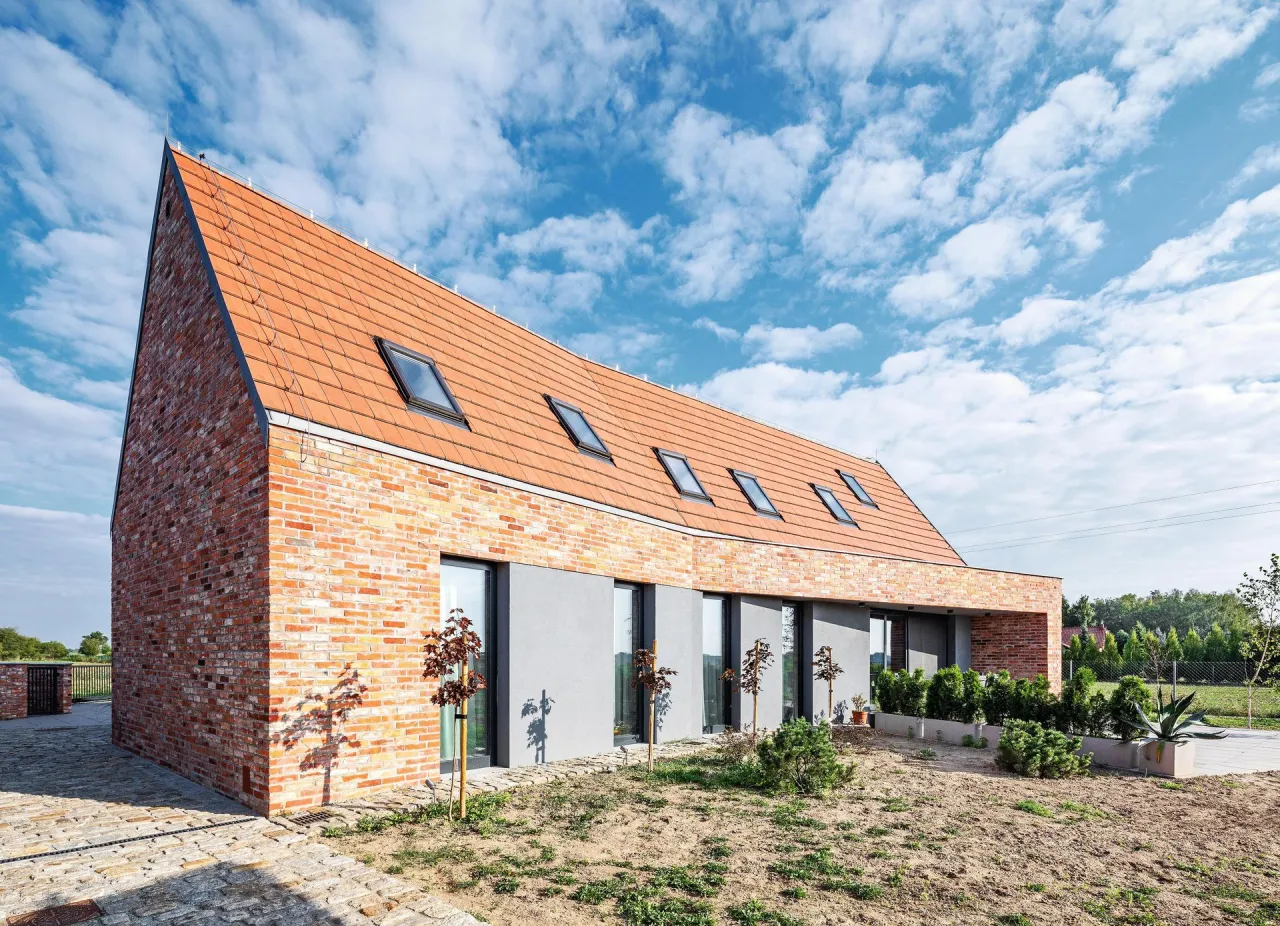 Nowoczesna elewacja domu z cegły i tynku, z ceramicznym dachem i oknami dachowymi.