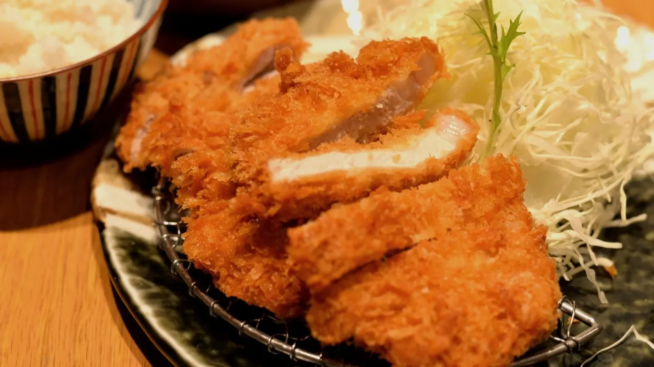 Chrupiący schabowy w panko, pokrojony na kawałki, podany z poszatkowaną kapustą i miseczką ryżu.