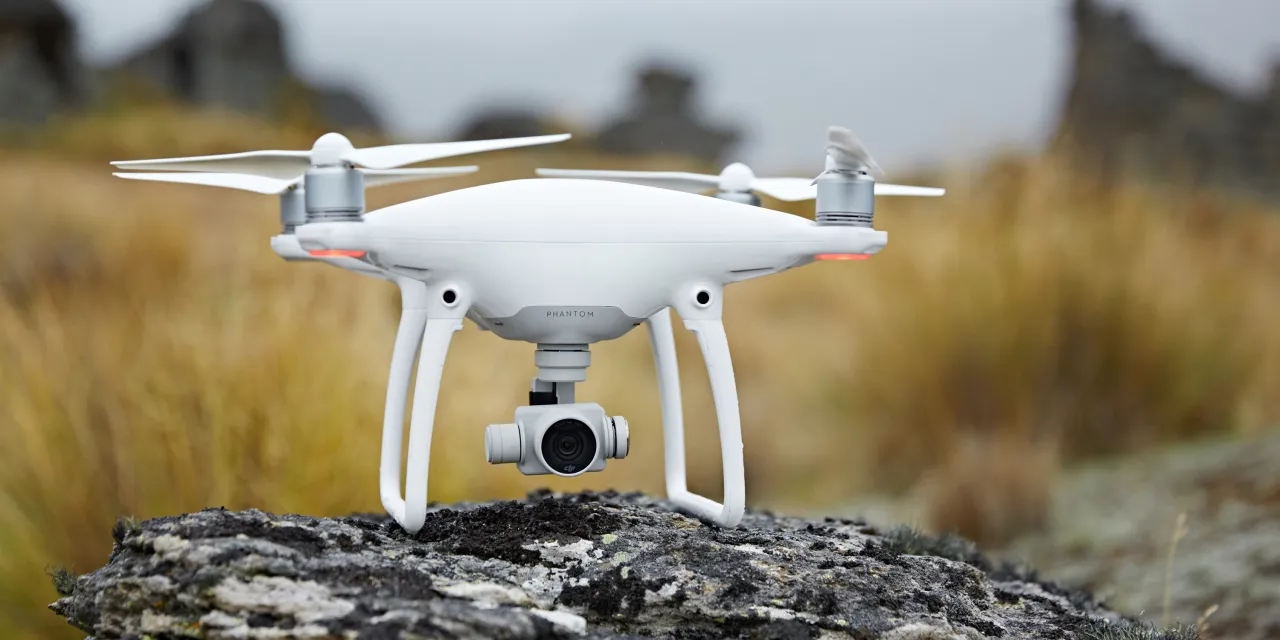 Biały dron Phantom z kamerą na kamieniu, gotowy do lotu. Fotograf wykorzystuje go do ujęć z powietrza.