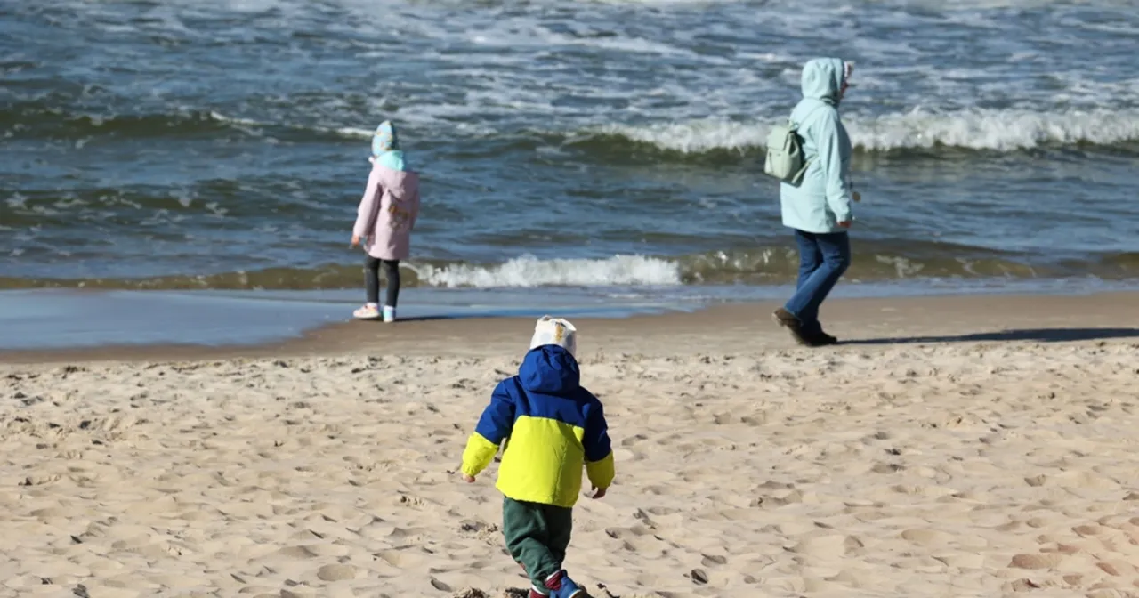 Rodzina na zimowej plaży nad Bałtykiem, dzieci w ciepłych ubraniach, pusta plaża