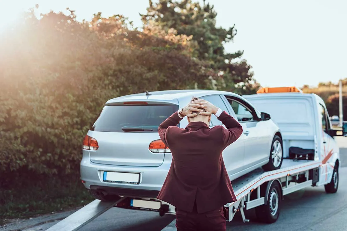 Zrozpaczony mężczyzna patrzy, jak jego auto jest ładowane na lawetę. Zastanawia się, co zrobić, żeby komornik nie zajął samochodu.