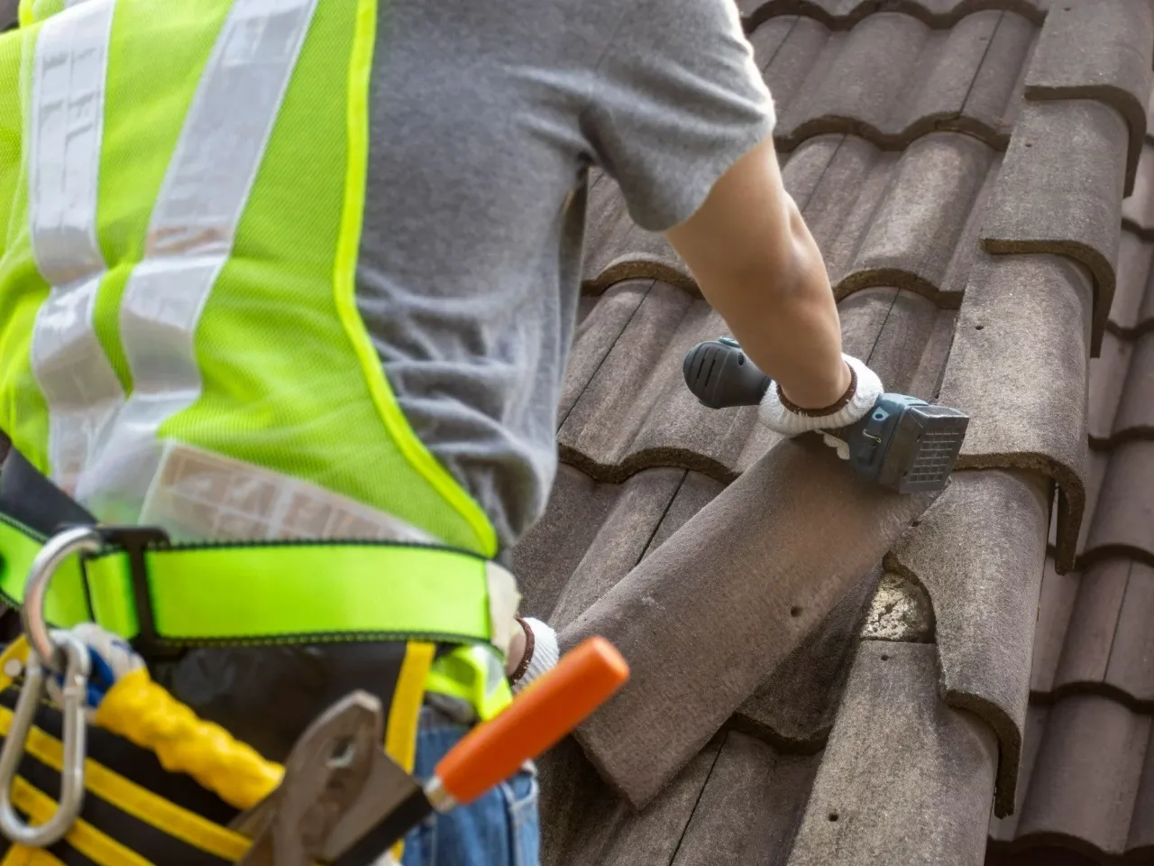 Pracownik w kamizelce odblaskowej na dachu z dachówką. Czy na ocieplenie dachu można dostać dofinansowanie?