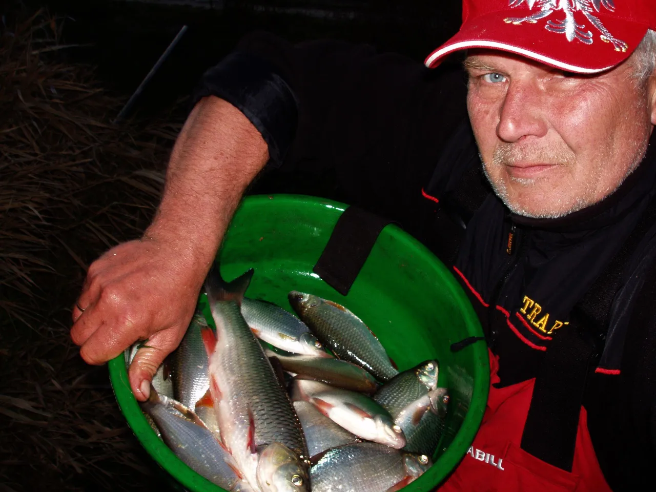 Wędkarz z pełnym wiadrem ryb, gotowy do przygotowania zanęty na ryby.