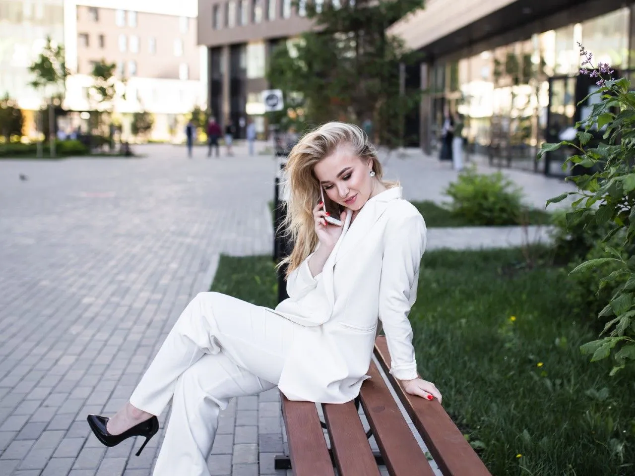 Kobieta w białym garniturze rozmawia przez telefon, zastanawiając się, jaka bluzka do białego garnituru będzie najlepsza.