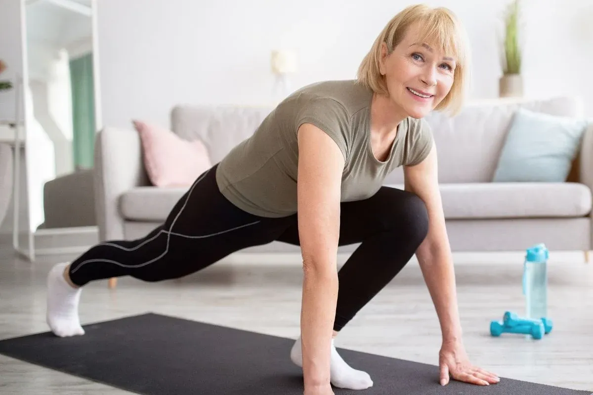Uśmiechnięta kobieta w średnim wieku ćwiczy w domu, pokazując, że można ćwiczyć podczas okresu.