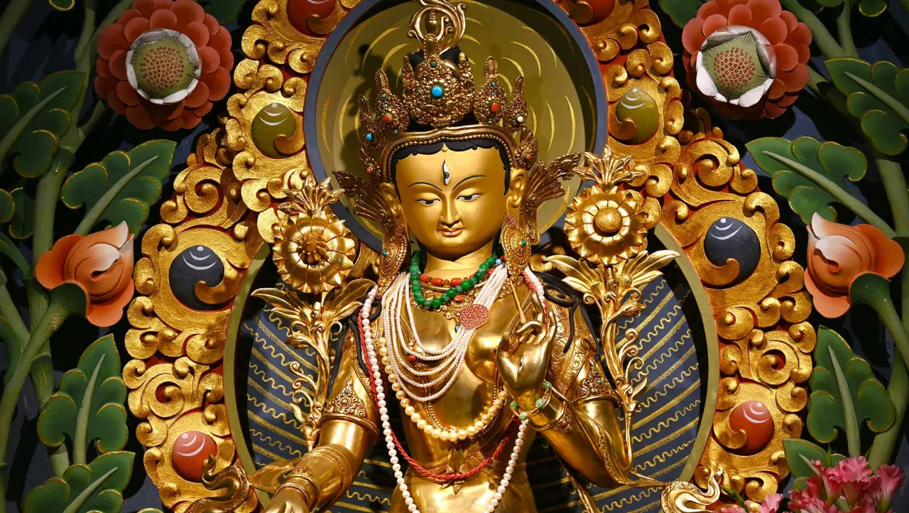 Złota statua Buddy w otoczeniu bogatych zdobień, gdzie dominuje buddyzm. Kwiaty i liście dodają jej uroku.