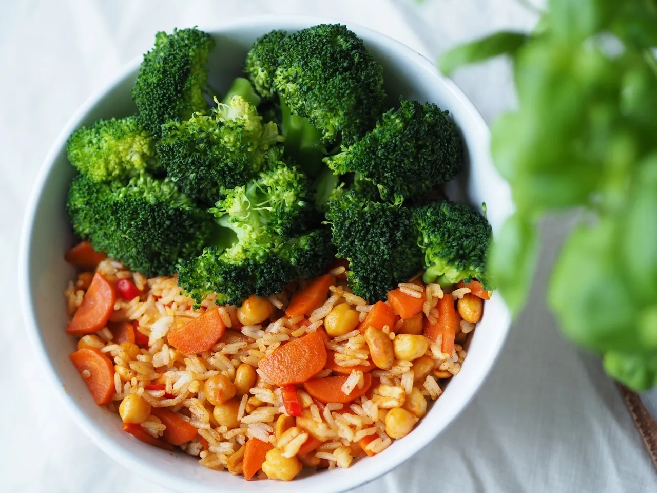 Kolorowy ryż z ciecierzycą i marchewką, przykryty zielonym brokułem. To zdrowy obiad wegański vs obiad normalny.