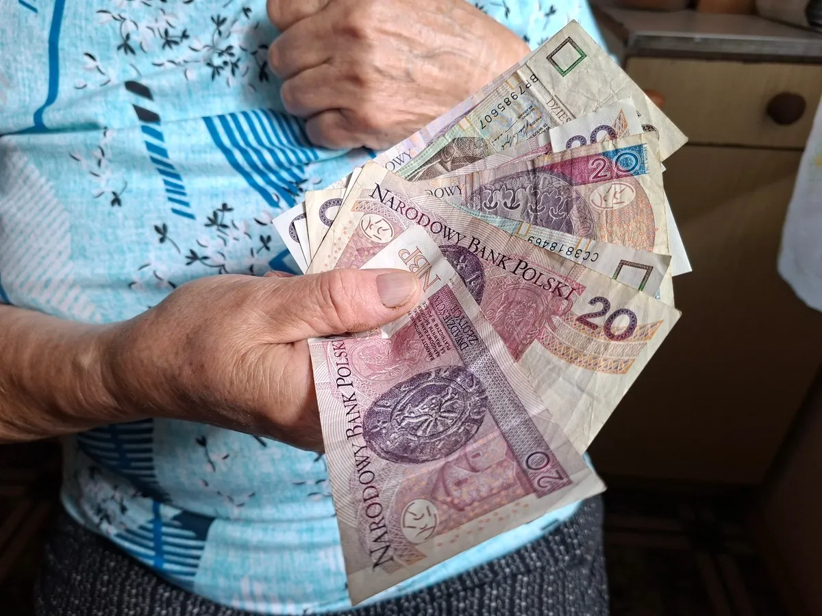 Dłoń trzyma polskie banknoty, symbolizujące rozważania, jak wybrać najkorzystniejsze lata do emerytury.