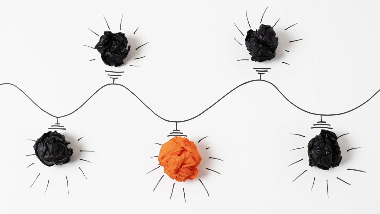 Pomarańczowa kulka papieru wśr&oacute;d czarnych, symbolizująca kluczowe podejmowanie decyzji i wyr&oacute;żniającą się ideę.