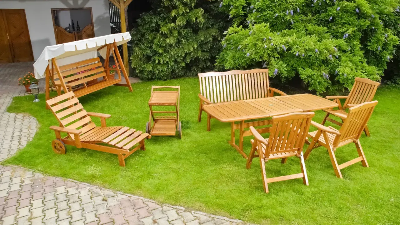 Drewniane meble ogrodowe: huśtawka, leżak, stół z krzesłami i wózek. Idealne na taras, gdy zastanawiasz się, jakie drewno na meble ogrodowe wybrać.