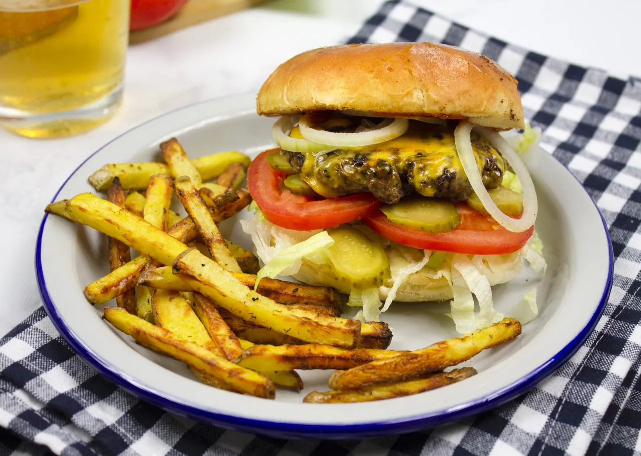 klasyczny hamburger z serem, sałatą, pomidorem, cebulą i sosem, na drewnianym tle