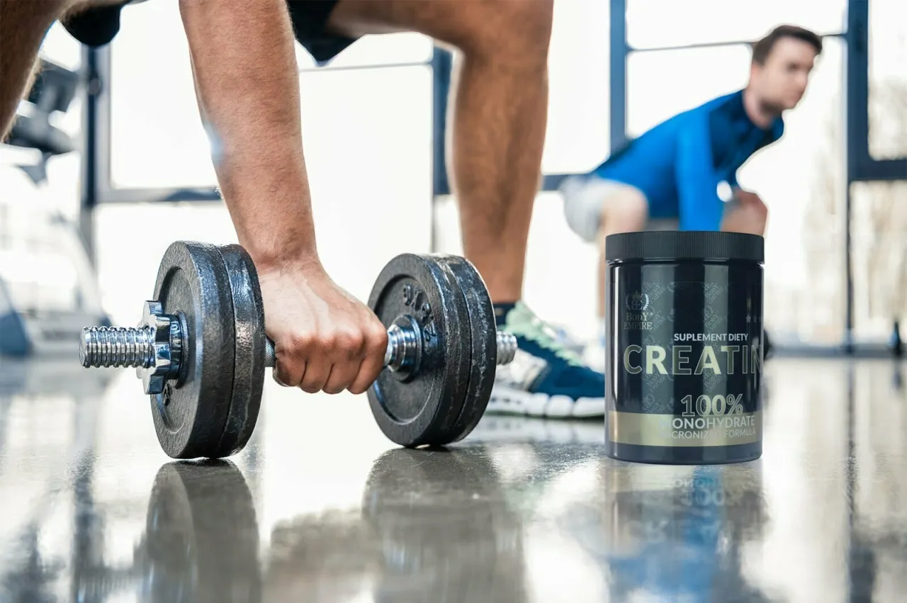 Mężczyzna podnosi ciężar, obok stoi puszka kreatyny. Kiedy brać kreatynę przed czy po treningu?