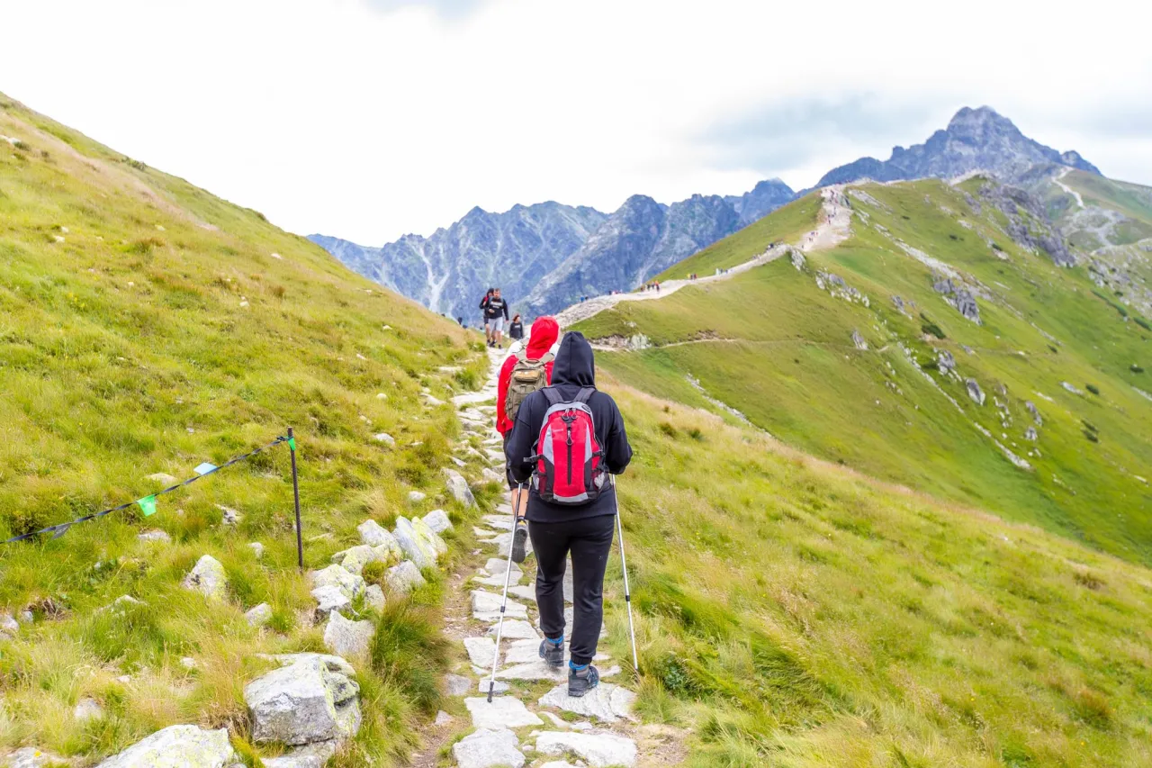 Grupa turyst&oacute;w wędruje kamienistym szlakiem po zielonych zboczach g&oacute;r. Idealne miejsce, gdzie w g&oacute;ry na maj&oacute;wkę.
