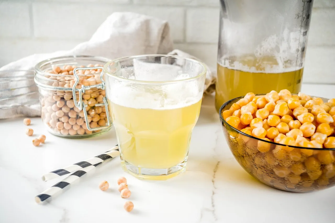 Aquafaba, płyn z ciecierzycy, idealny do deserów co zamiast surowych jaj. Szklanka z pianką, miska i słoik pełne ciecierzycy.