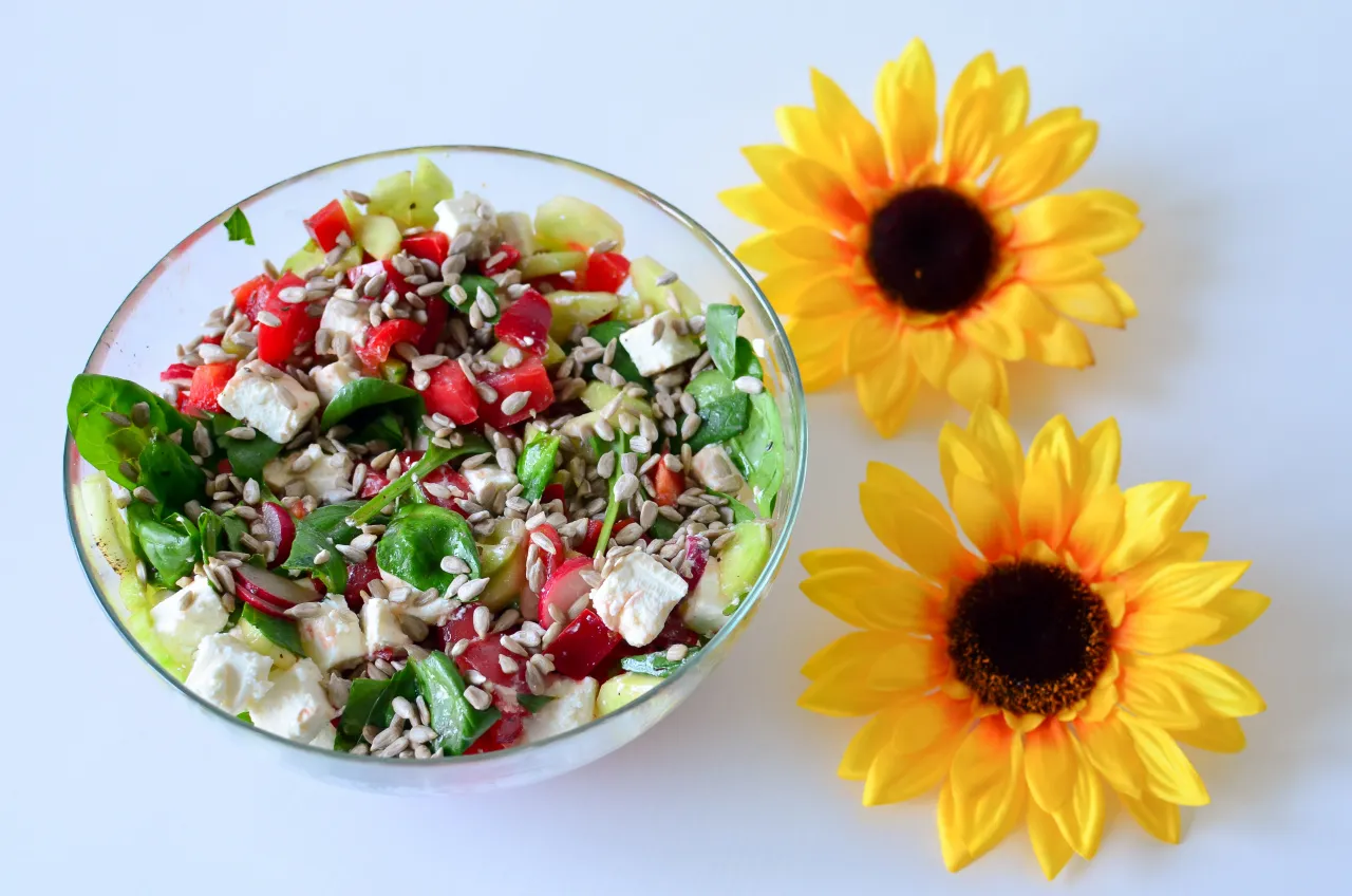Kolorowa sałatka ze szpinakiem, fetą, pomidorami i chrupiącym słonecznikiem, obok dwóch żółtych słoneczników.