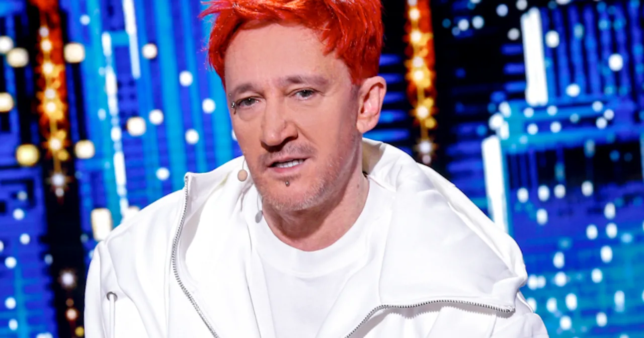 Michał Wiśniewski z charakterystycznymi rudymi włosami i piercingiem na twarzy, w białej bluzie. Choć nie widać tego na zdjęciu, jego wzrost to 175 cm.