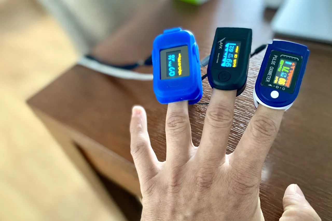 Trzy pulsoksymetry na palcach pokazują wyniki, potwierdzając prawidłową saturację u dziecka.