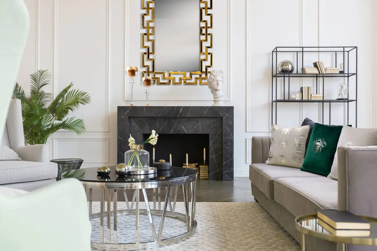 Elegancki salon z marmurowym kominkiem, złotym lustrem i wygodną sofą. Inspiracja, jak udekorować kominek, by stworzyć przytulną atmosferę.