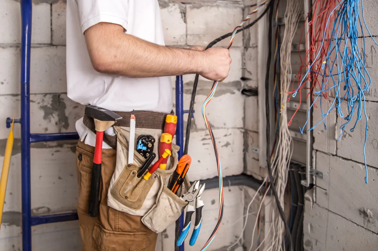 Elektryk z pasem narzędziowym sprawdza, jakie obciążenie wytrzyma przewód 1,5 mm², wśród plątaniny kolorowych kabli.