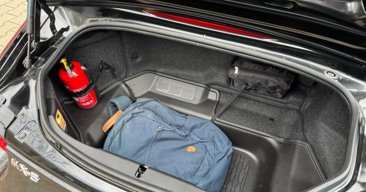 W bagażniku MX-5 znajduje się gaśnica, kt&oacute;ra zapobiega mandatowi za brak gaśnicy. Obok leży niebieski plecak i czarna torba.