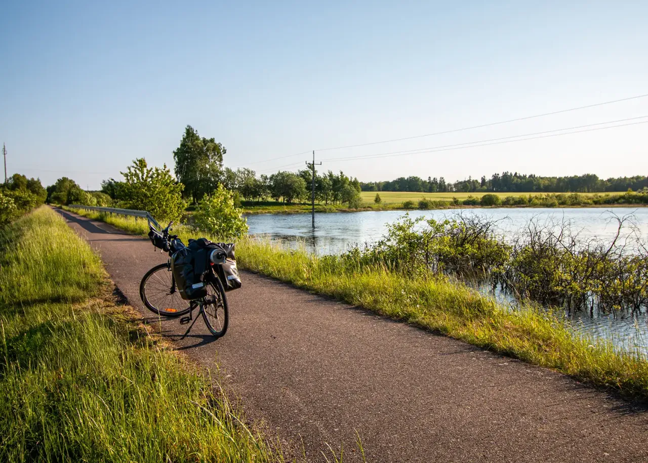 Rower z sakwami na ścieżce rowerowej wokół jeziora. Słoneczny dzień, zieleń traw i drzew.