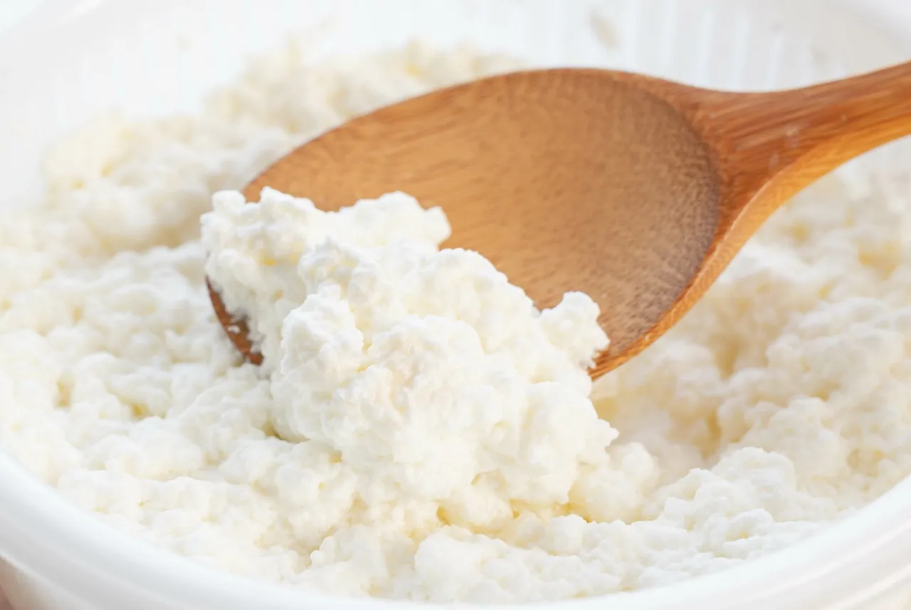 Świeży twaróg w wiaderku, nabierany drewnianą łyżką. Czy można mrozić twaróg w wiaderku? Tak, można go mrozić.