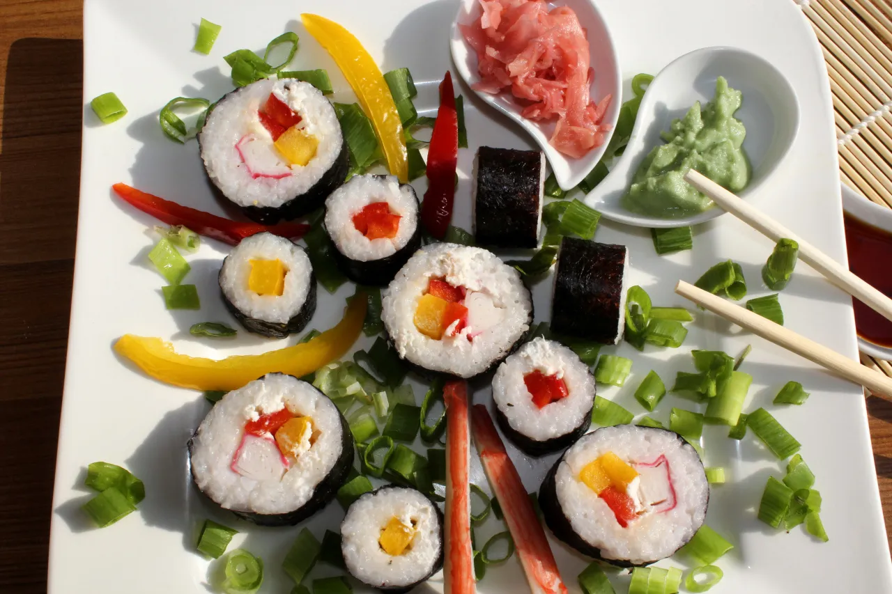 Kolorowe rolki sushi z surimi, papryką i szczypiorkiem, podane z wasabi i imbirem.