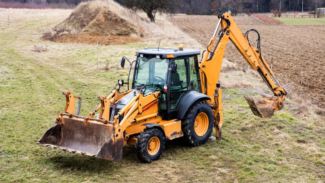 Pomarańczowa koparko-ładowarka na placu budowy, gotowa do egzaminu na koparko ładowarki.