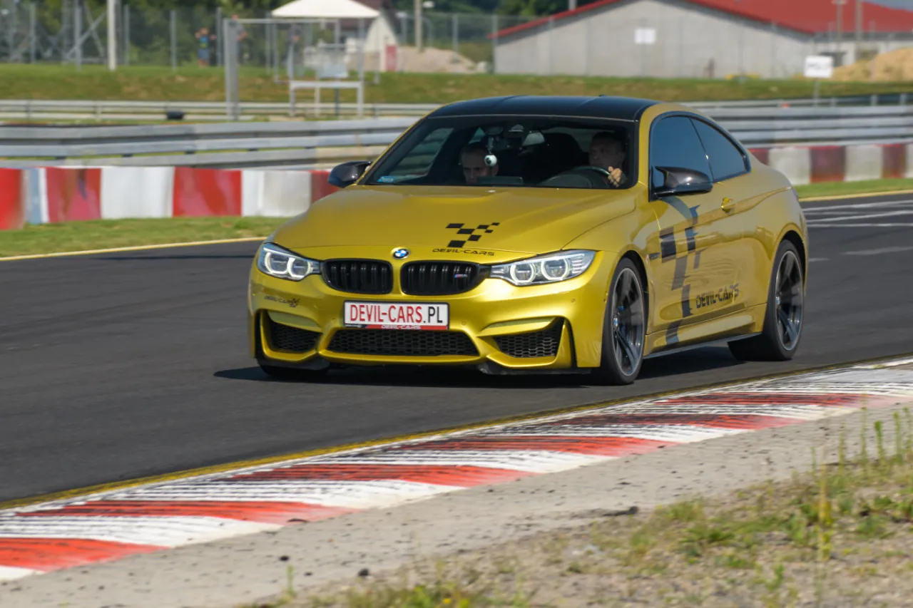 Złote BMW M4 z tablicą DEVIL-CARS.PL na torze wyścigowym. Kierowca i pasażer cieszą się jazdą po torze swoim samochodem.