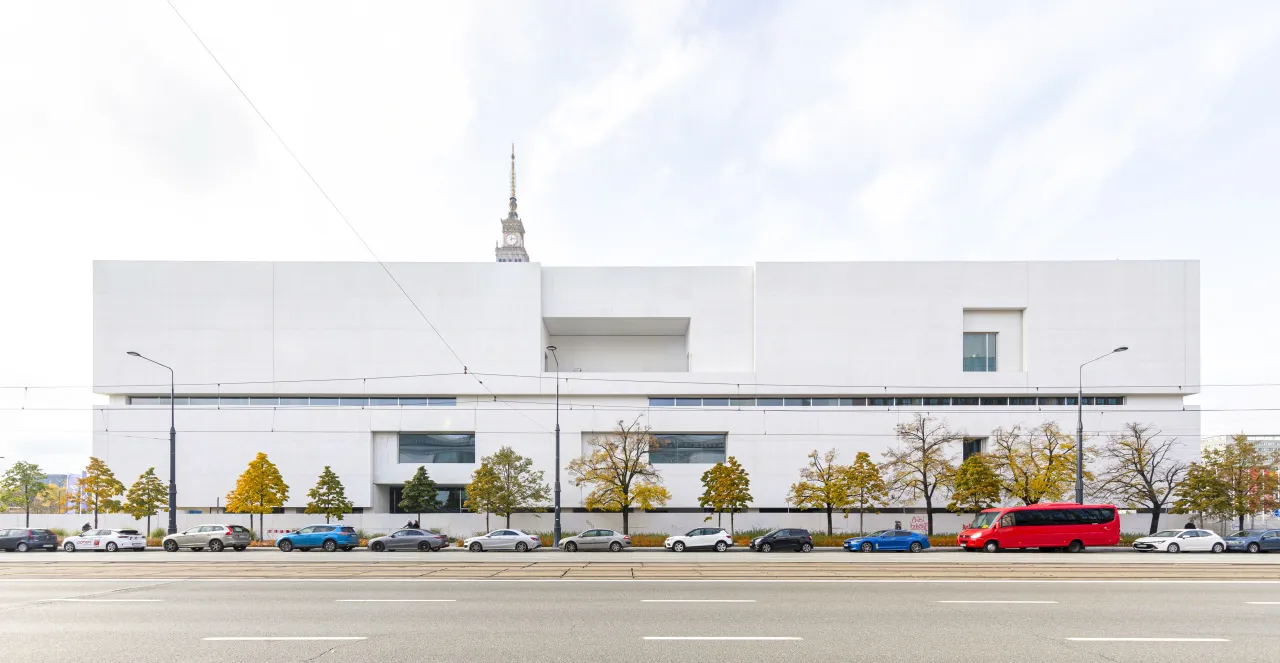 Nowoczesne muzeum sztuki nad Wisłą, z charakterystyczną białą fasadą i drzewami w jesiennych barwach.