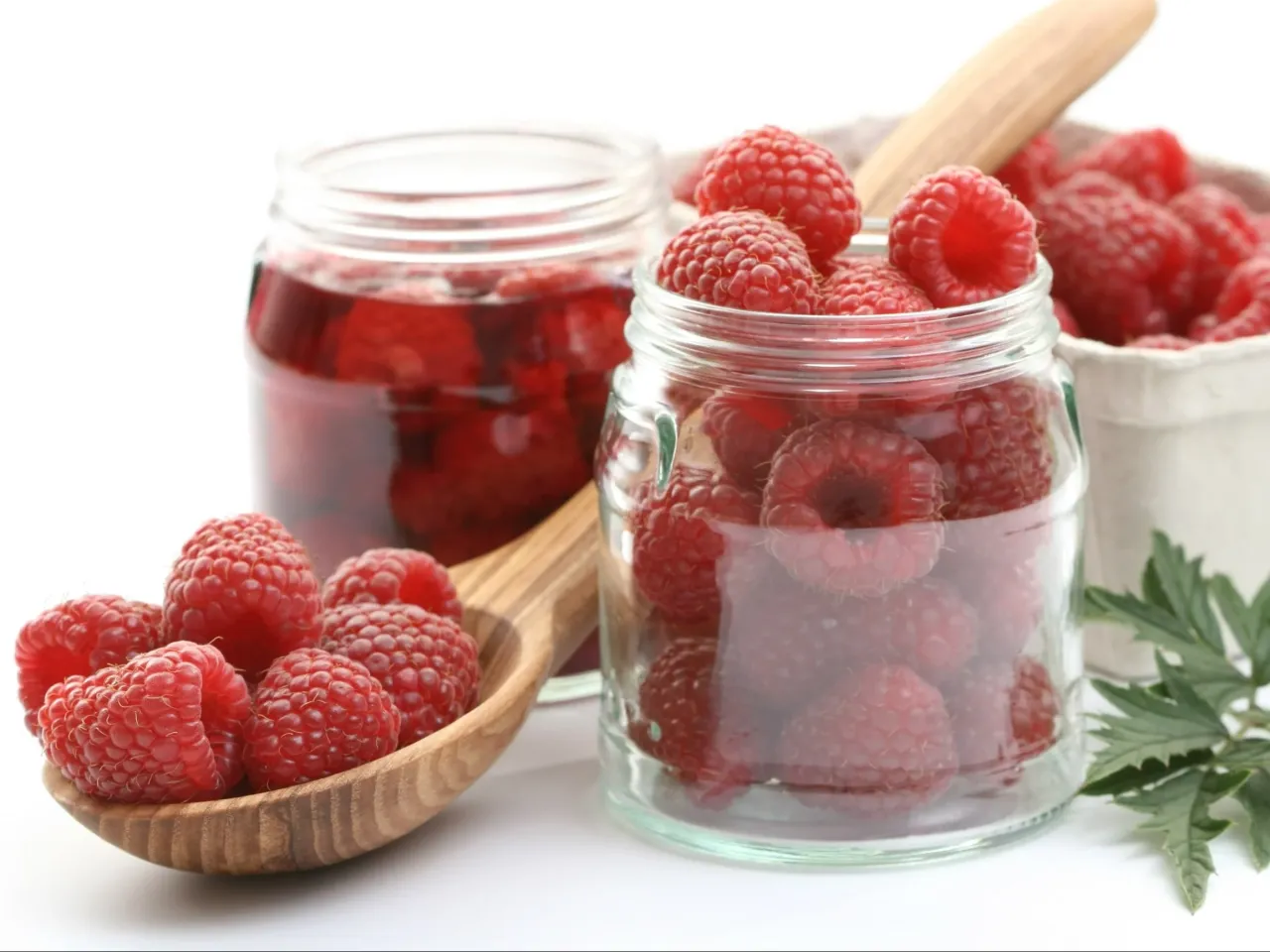 Słoiki z malinami i drewniana łyżka. Idealne składniki, by dowiedzieć się, jak zrobić sok z malin na surowo.