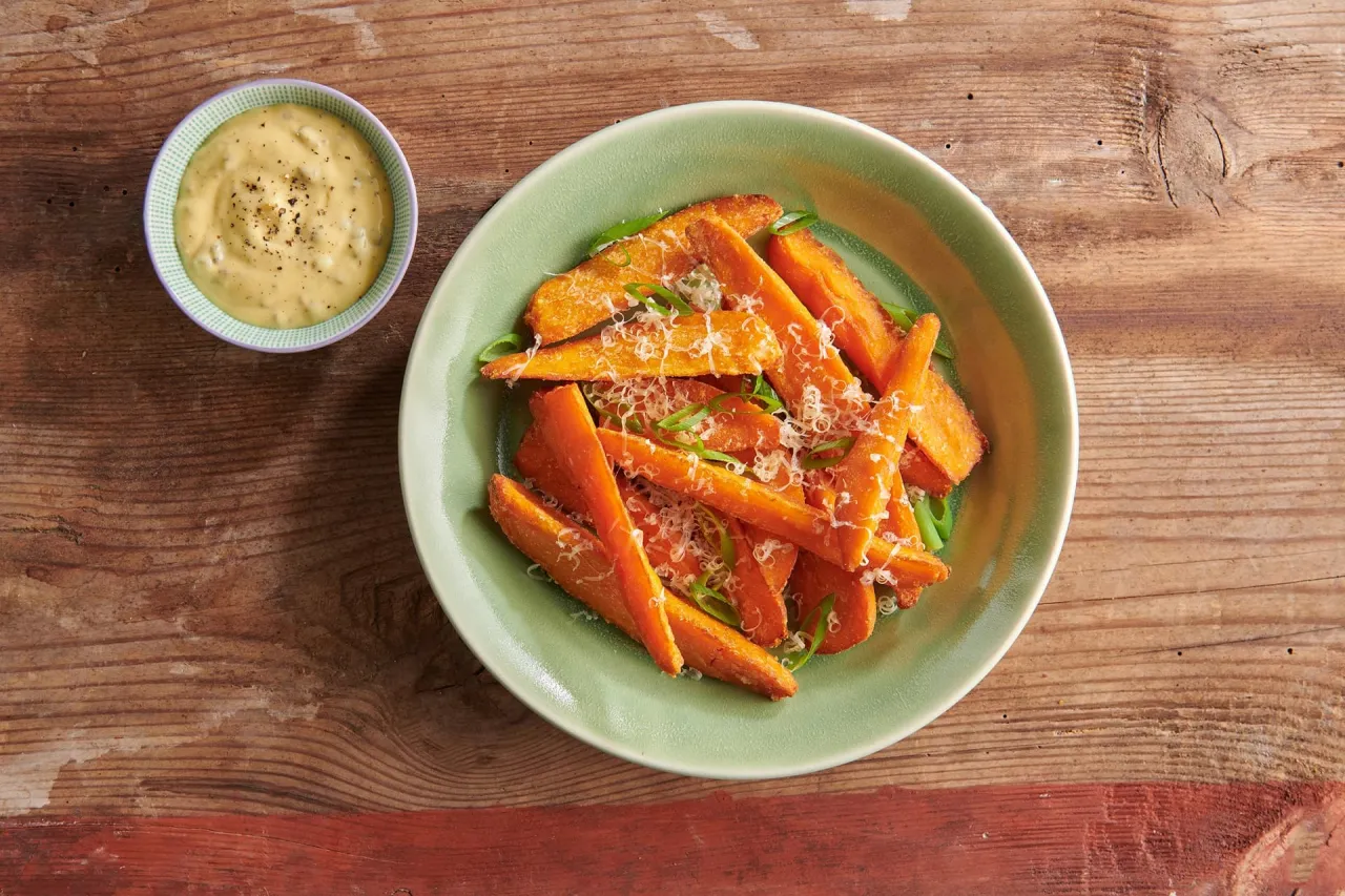 Pomarańczowe frytki z batat&oacute;w posypane parmezanem i szczypiorkiem, idealne co do frytek na szybko, z sosem w miseczce obok.