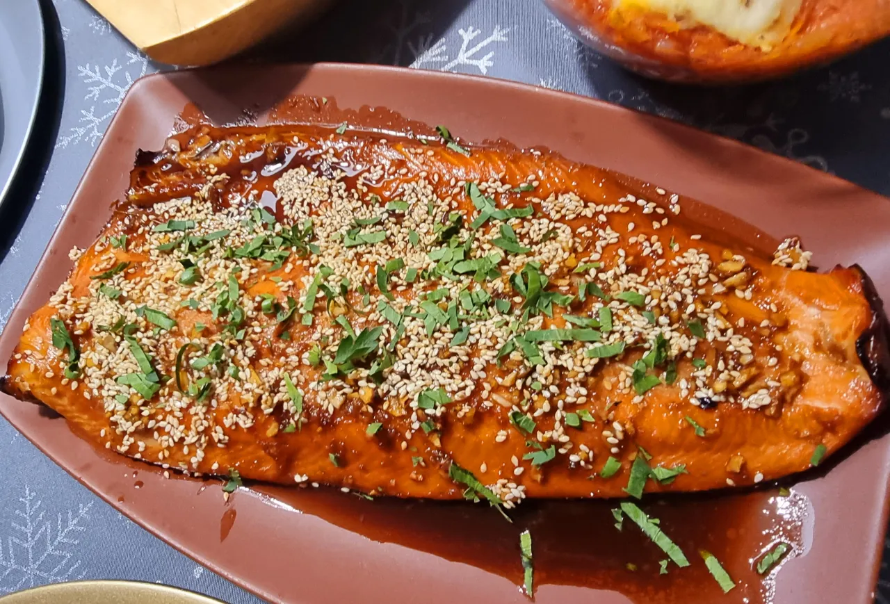 Pyszny łosoś w sosie sojowym, posypany sezamem i natką pietruszki, prezentuje się apetycznie na brązowym talerzu.