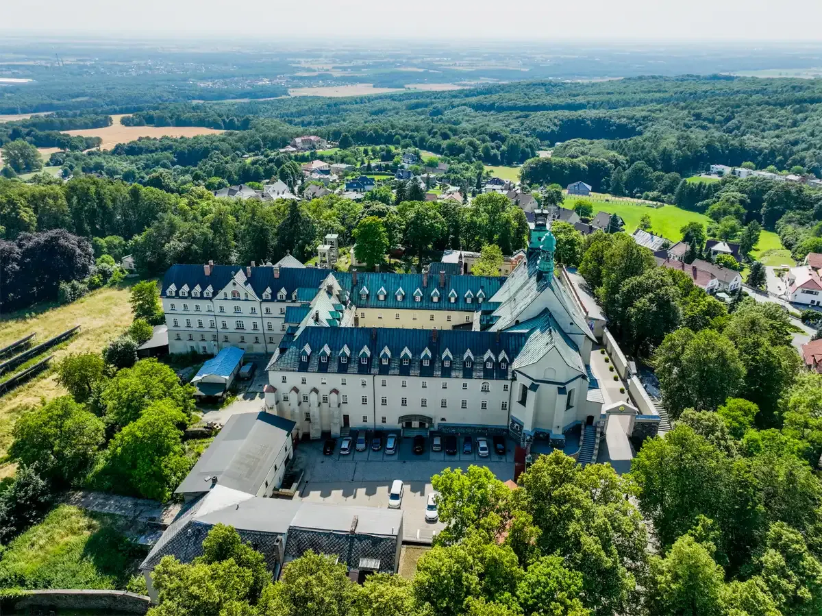 Widok z lotu ptaka na klasztor na G&oacute;rze Świętej Anny, otoczony zielenią i polami.