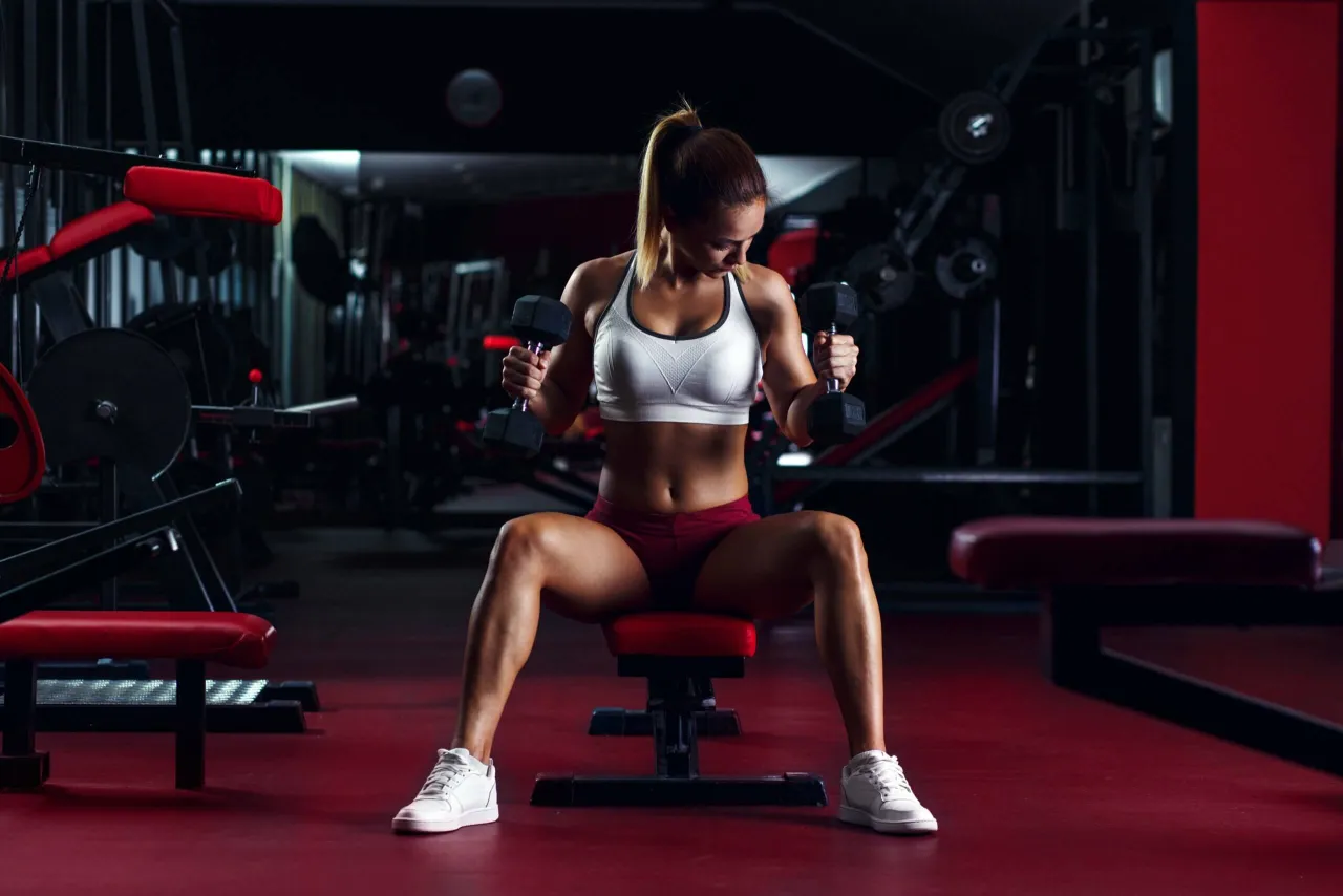 Kobieta ćwiczy z hantlami na siłowni. Czy crossfit pomaga schudnąć? Intensywny trening buduje mięśnie i spala kalorie.