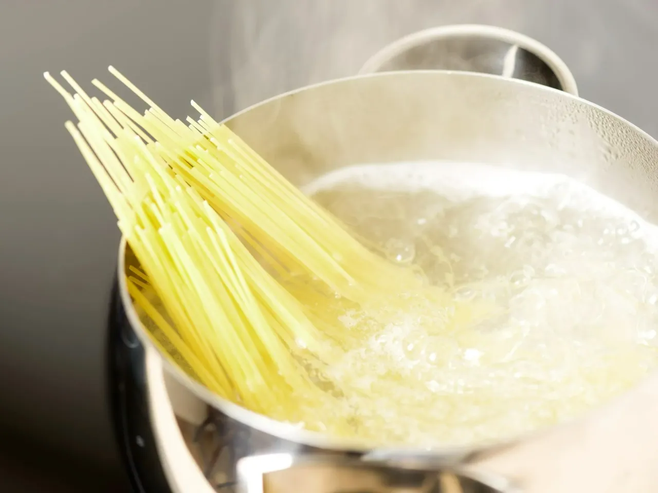 kucharz wylewający olej do garnka z makaronem