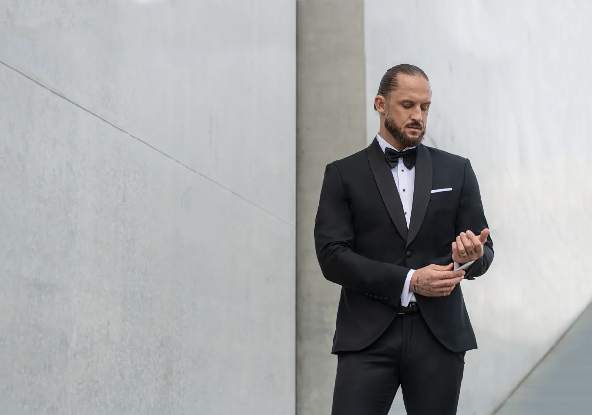 Elegancki mężczyzna w smokingu, idealny przykład stroju black tie, kontrastuje z luźniejszym stylem cocktail dress dla gości weselnych.