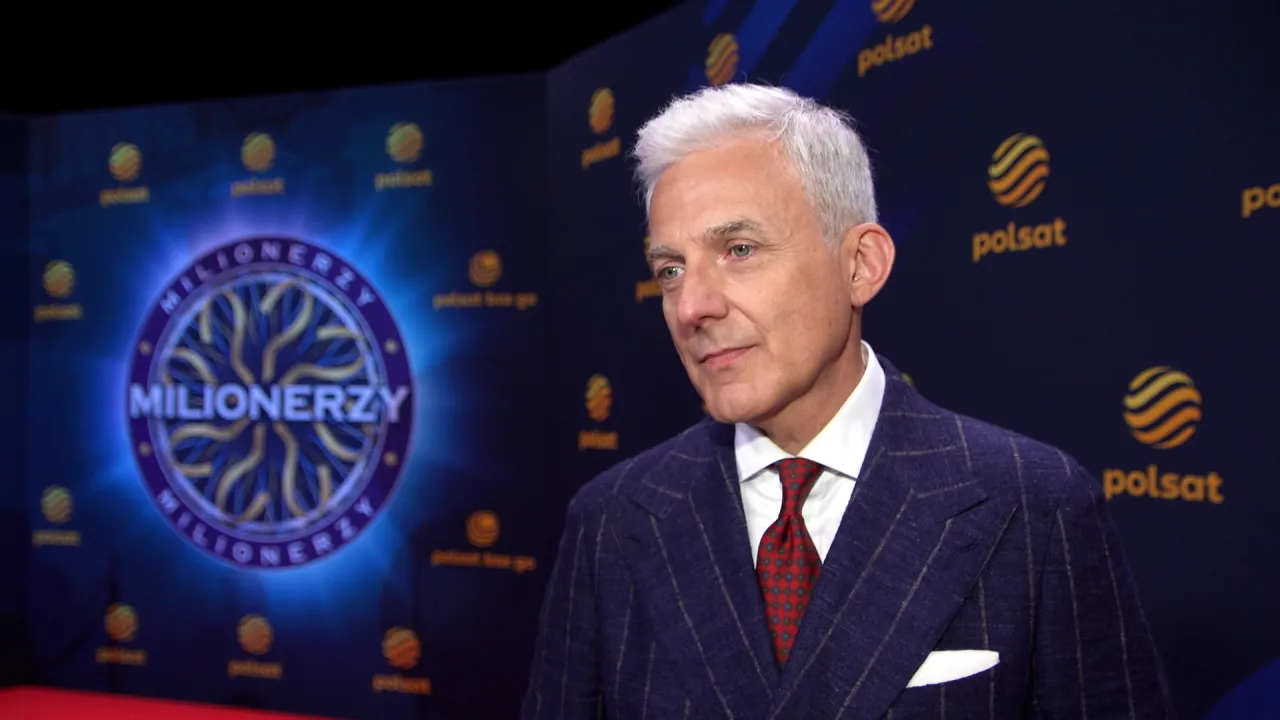 Hubert Urbański w garniturze, na tle logo 